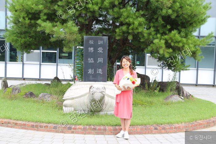 김광자 선생님이 꽃다발을 들고 기념비를 배경으로 서 있다.