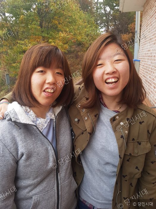 두 여성이 밝은 미소를 지으며 나란히 서 있다.