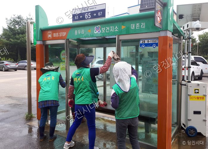 봉사자들이 버스정류장 유리를 깨끗이 닦고 있다.