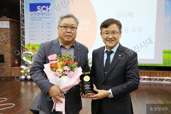 두 남성이 대학 행사에서 감사패와 꽃다발을 들고 기념 촬영을 하고 있다.