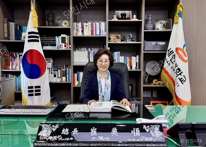 최미순 총장이 사무실 책상에 앉아 책을 펼쳐 보며 미소를 짓고 있다.
