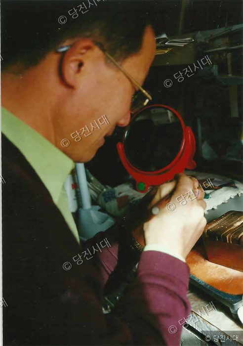 한 남성이 작업대에서 세심한 손길로 공예품을 만들고 있다.