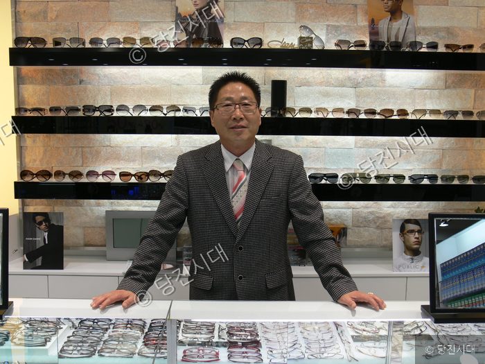 안경원 점장이 매대 앞에 서서 포즈를 취하고 있다.