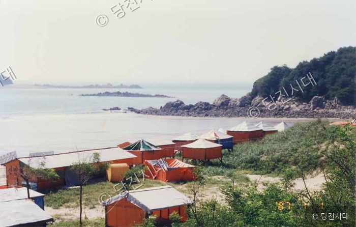 바닷가 백사장에 주황색 지붕의 텐트들이 늘어서 있다.