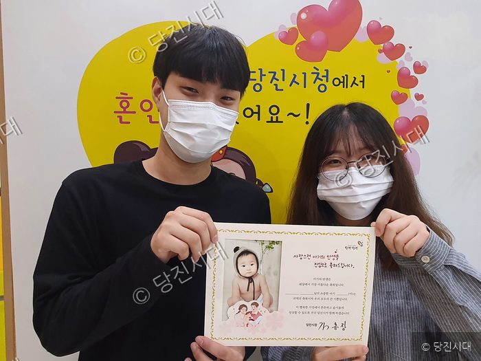 한 남녀가 당진시의 아기 출생 축하 카드를 들고 기념 촬영을 하고 있다.