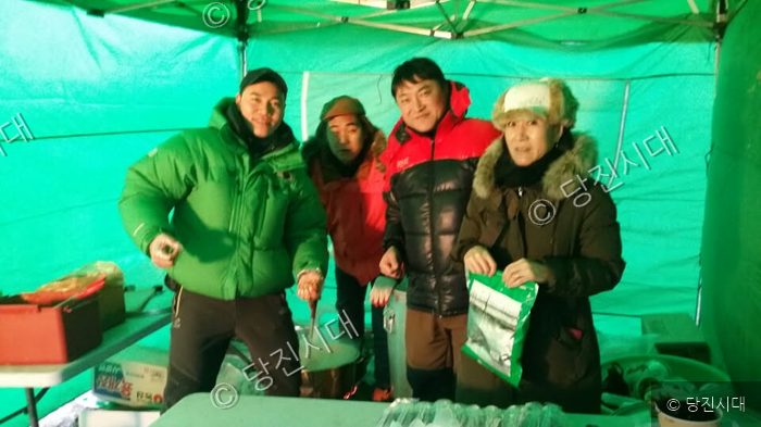 네 명의 주민이 녹색 텐트 안에서 밝은 표정으로 서 있다.