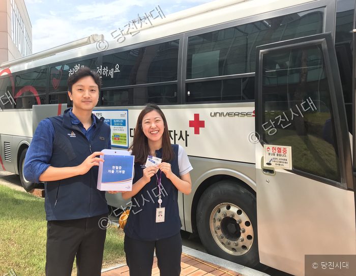 직원들이 헌혈 버스 앞에서 헌혈증 기부함을 들고 포즈를 취하고 있다.