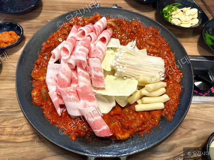 철판 위에 양념된 쭈꾸미와 삼겹살, 채소가 푸짐하게 올려져 있다.