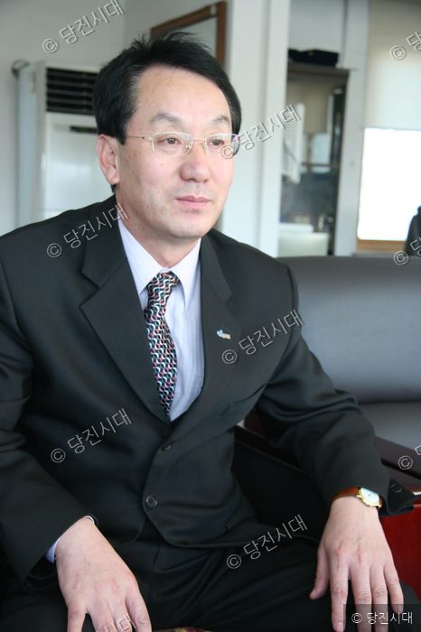 홍사현 송악면장이 인터뷰를 위해 정장 차림으로 앉아 포즈를 취하고 있다.