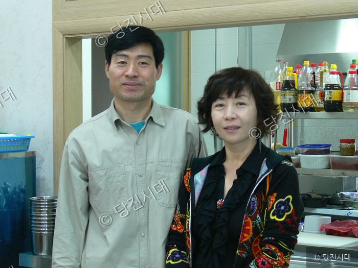 식당을 운영하는 부부가 주방 앞에서 포즈를 취하고 있다.