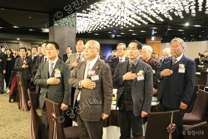 참석자들이 실내 행사에서 가슴에 손을 얹고 있다.