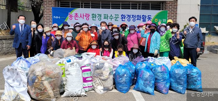 주민들과 관계자들이 수거한 쓰레기 봉투 뒤에서 환경정화활동 기념 사진을 찍고 있다.
