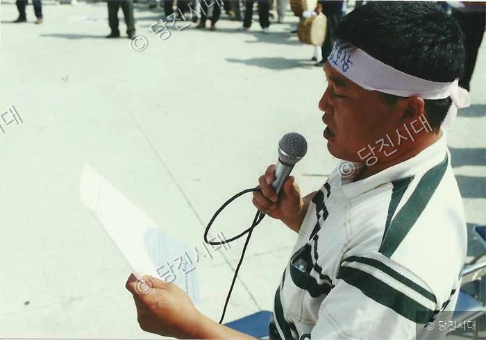 한 남성이 머리에 띠를 두르고 마이크를 든 채 문서를 읽고 있다.