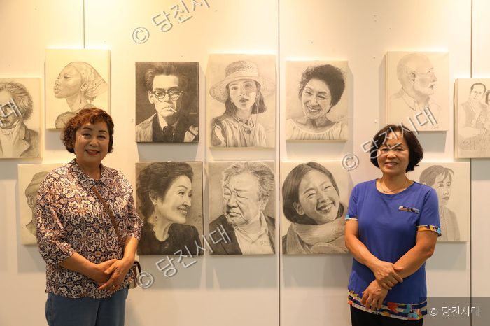 연필 초상화 전시회장에서 두 여성이 포즈를 취하고 있다.