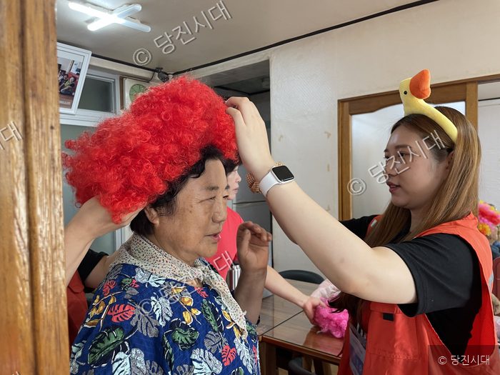 자원봉사자가 마을 어르신에게 가발을 씌워드리고 있다.