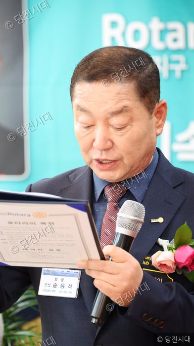 한 남성이 마이크를 들고 로타리 클럽 관련 문서를 낭독하고 있다.