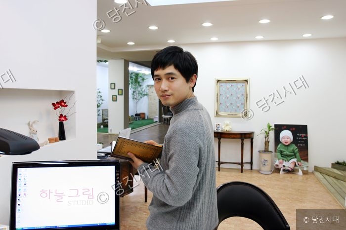 스튜디오에서 홍승표 씨가 책을 들고 카메라를 응시하고 있다.