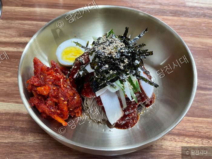 식당에서 메밀국수 한 그릇이 먹음직스럽게 담겨 있다.