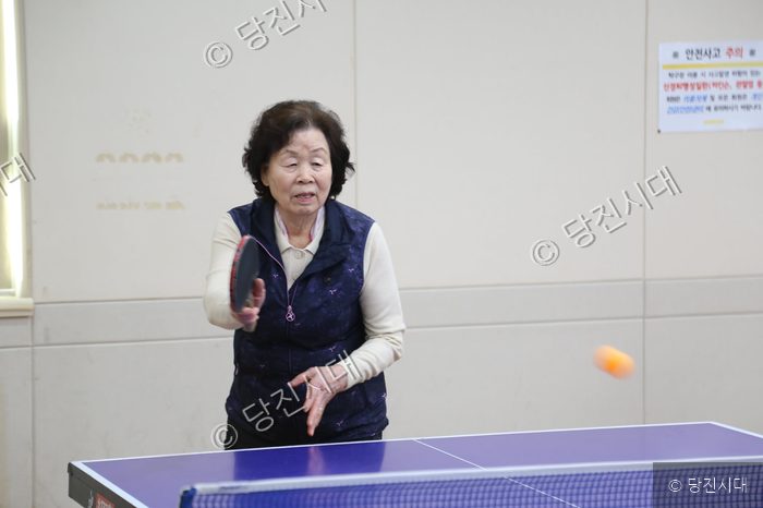 어르신이 탁구대 앞에서 탁구를 치고 있다.