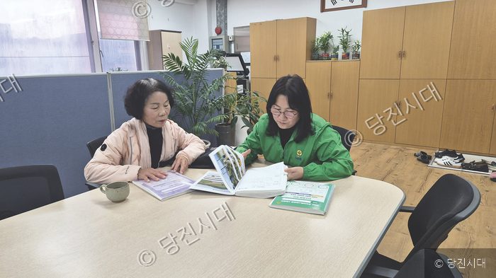 사무실에서 두 사람이 문서와 책을 함께 살펴보며 이야기를 나누고 있다.