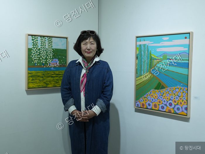 미술 전시회장에서 작가가 자신의 그림 작품들 앞에 서 있다.