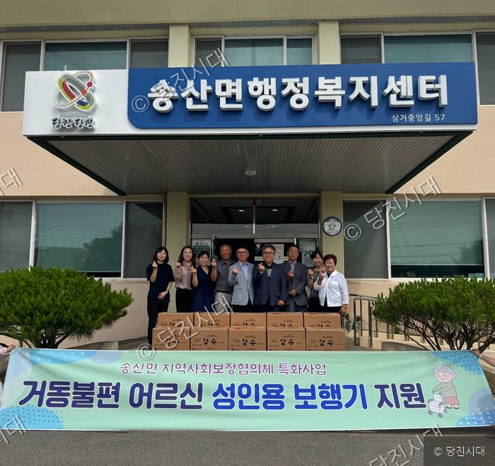 송산면행정복지센터 앞에서 관계자들이 거동불편 어르신 성인용 보행기 지원 기념 촬영을 하고 있다.