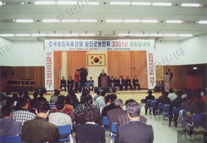사람들이 강당에서 농민회 관련 행사에 참석하여 앉아 있다.