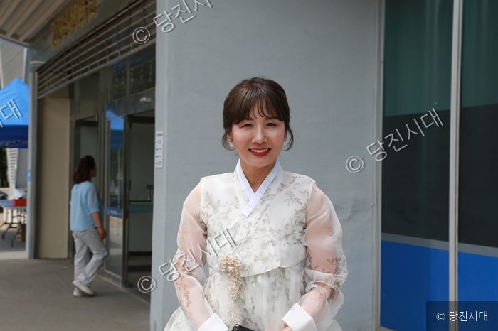 한복을 입은 여성이 건물 앞에서 미소를 지으며 카메라를 바라보고 있다.