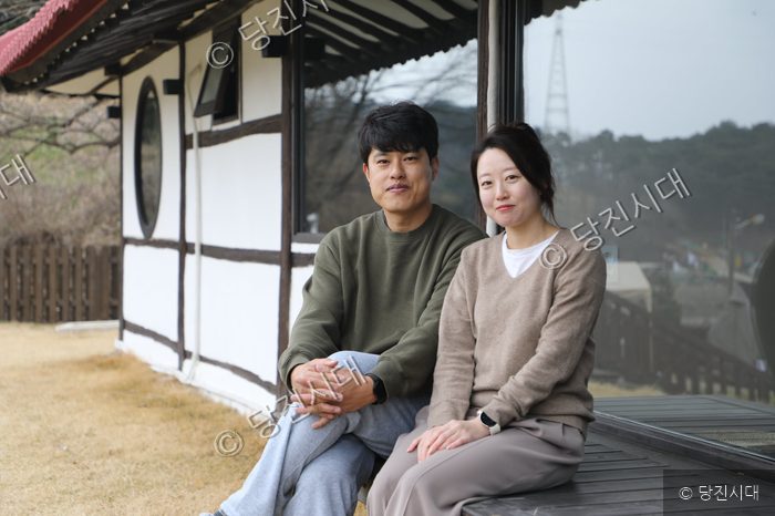 산아래펜션을 운영하는 부부가 펜션 앞에 나란히 앉아 미소 짓고 있다.