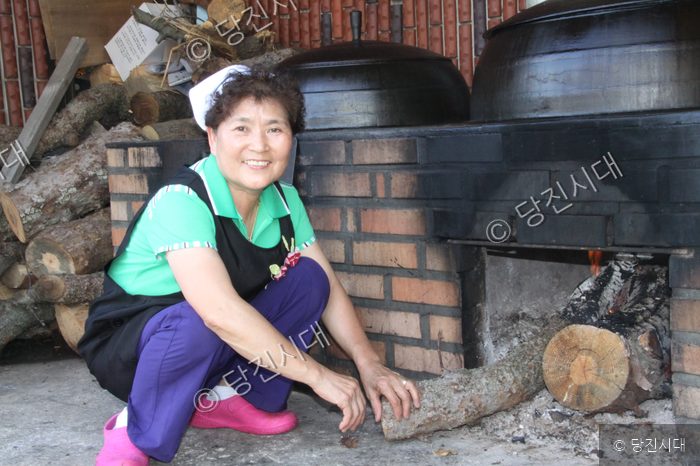 여성 대표가 가마솥이 있는 아궁이 앞에 쭈그리고 앉아 있다.