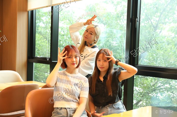 해나루 퀸즈 동아리 회원 세 명이 다정한 포즈로 카메라를 향해 웃고 있다.