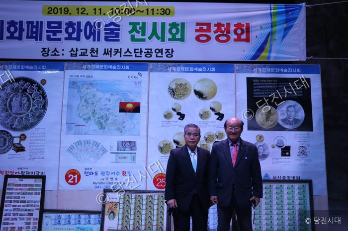 두 남자가 세계화폐문화예술전시회 공청회 현장에서 포즈를 취하고 있다.