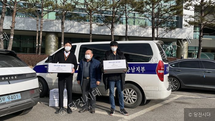 세 명이 차량 앞에서 선물 상자를 들고 기념 촬영을 하고 있다.