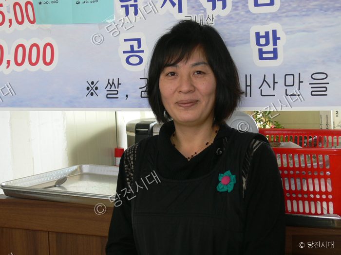 식당을 운영하는 업주가 카메라를 향해 미소 짓고 있다.