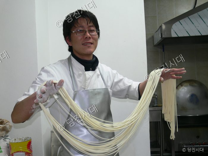 요리사가 주방에서 수타면을 길게 늘여 보여주고 있다.