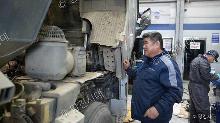 정비사가 대형 트럭의 엔진을 점검하고 있다.