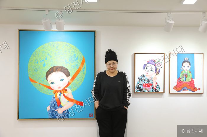 미술관에서 작가가 자신의 작품들 앞에 서서 포즈를 취하고 있다.