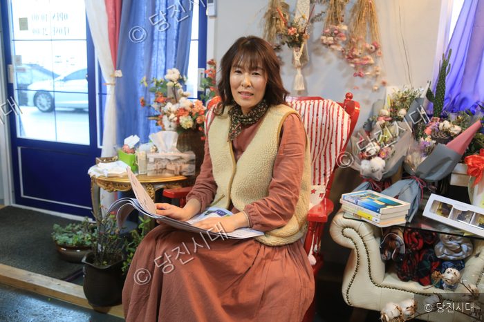 이선숙 대표가 꽃집 내부에서 카탈로그를 보며 미소 짓고 있다.