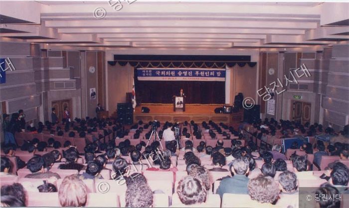 강당에서 많은 사람들이 모인 가운데 국회의원 후원의 밤 행사가 열리고 있다.
