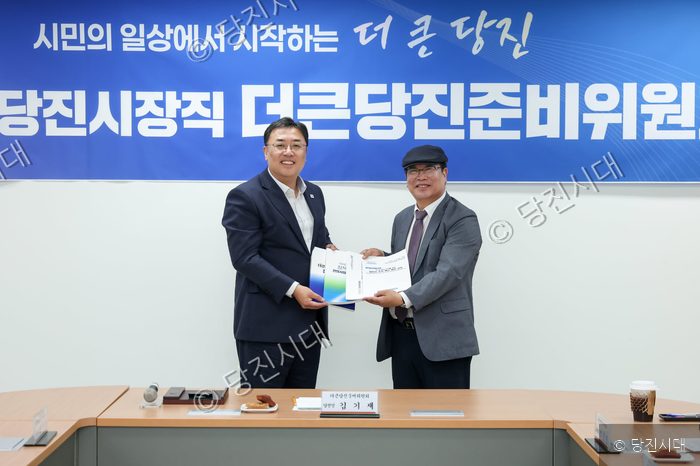 두 사람이 시정 운영 제안서가 담긴 서류를 함께 들고 기념 촬영을 하고 있다.