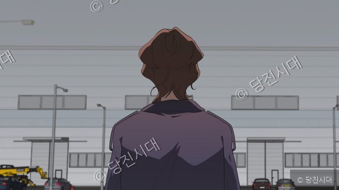 주인공이 공장 앞에서 앞모습을 보이며 서 있다.