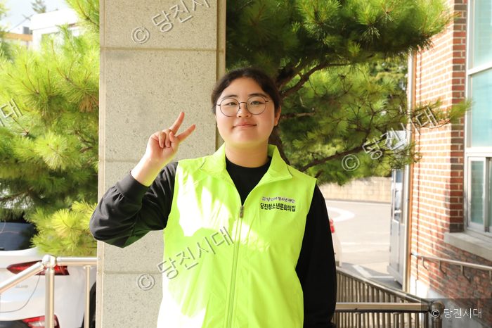 안경을 쓴 한 청소년이 형광 조끼를 입고 브이 포즈를 취하고 있다.