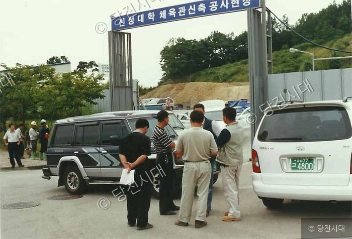 사람들이 신성대학 체육관 신축 공사 현장 입구에 모여 있다.