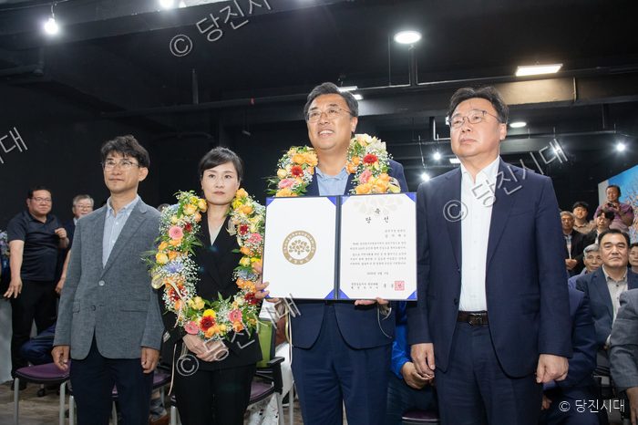 당선인이 화환을 걸고 당선증을 들어 보이며 기념 촬영을 하고 있다.