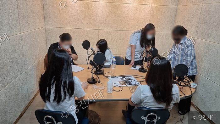 청소년들이 녹음실에서 마이크 앞에 모여 방송을 준비하고 있다.