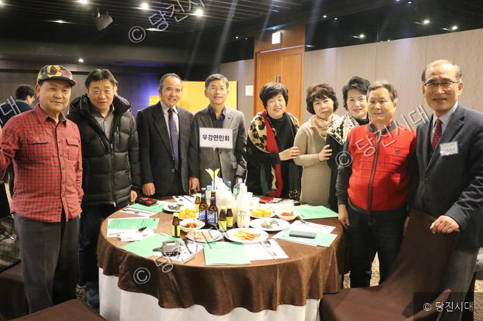 우강면민회 회원들이 테이블 주변에 모여 기념촬영을 하고 있다.