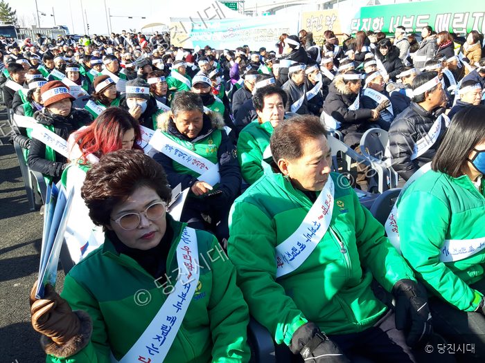 사람들이 모여 집회 현수막과 어깨띠를 착용하고 앉아 있다.