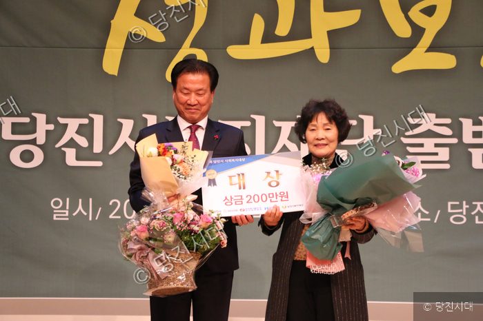 당진시 복지대상 시상식에서 수상자가 상패와 꽃다발을 들고 기념 촬영을 하고 있다.