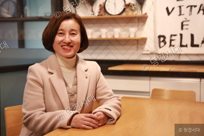 김진숙 민중당 당진시위원장이 카페 테이블에 앉아 밝은 표정으로 미소 짓고 있다.