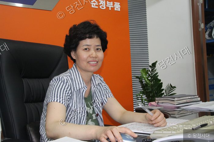 김금자 대표가 사무실 책상에 앉아 환하게 웃고 있다.